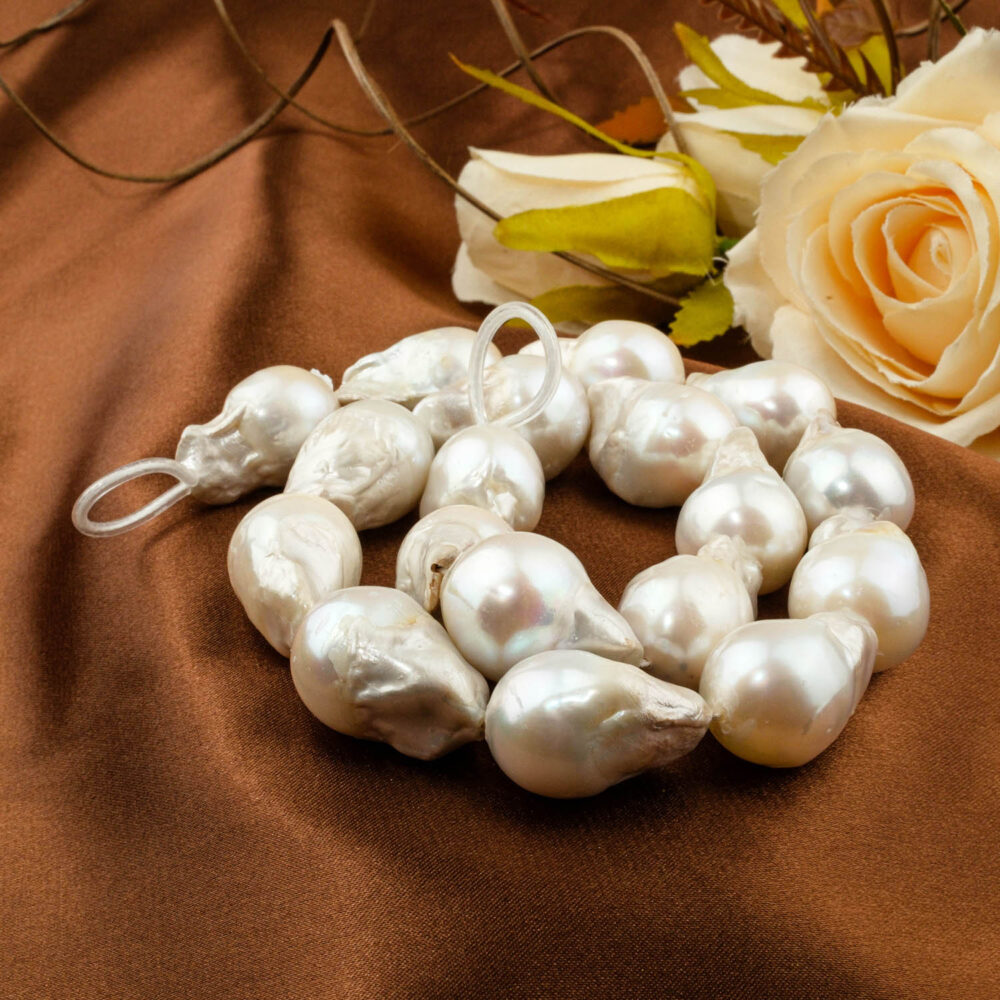 Strand of large irregular (baroque) white saltwater pearls, 16x23mm avg size, displayed on brown satin.