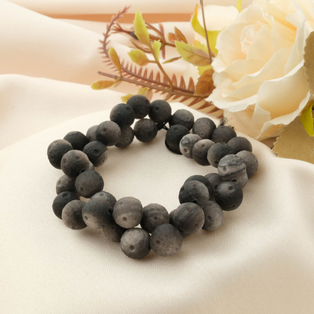 A special matte (frosted) Silver Sheen Obsidian bracelet with 8-9mm beads, styled on a cream satin cloth with a rose.