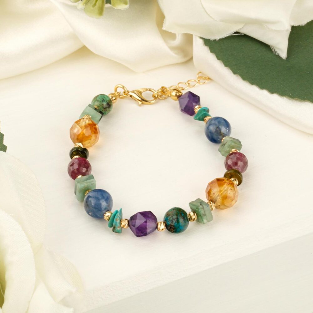 Mixed gemstone steel bracelet with emerald citrine peridot ruby sapphire amethyst and chrysocolla beads on white surface with flowers