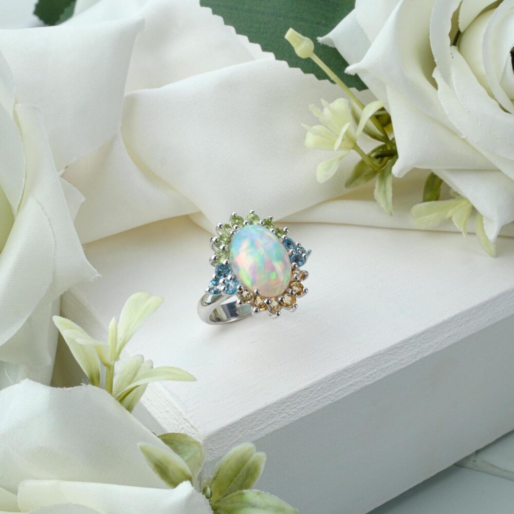 Ornate 925 sterling silver ring featuring an oval opal cabochon with a halo of blue topaz, citrine, and peridot on white
