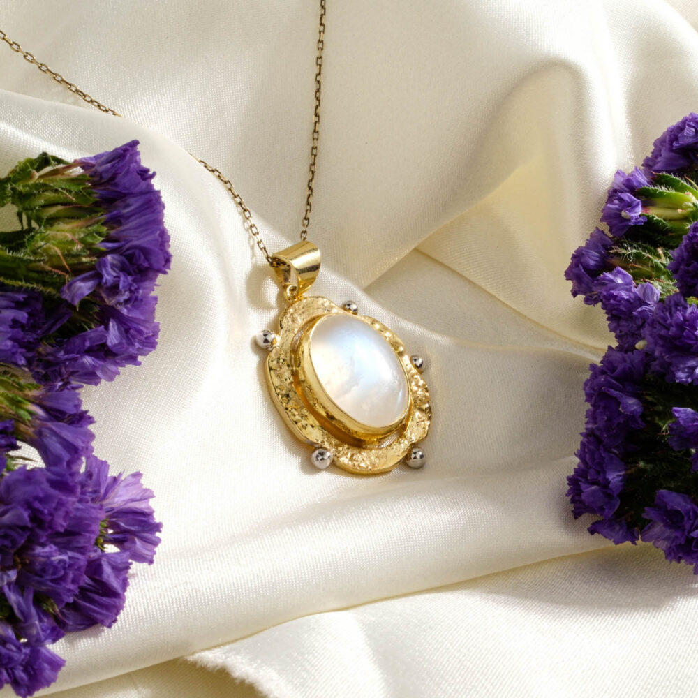 Ornate rainbow moonstone pendant with blue flash in a 925 silver gold-plated setting on white
