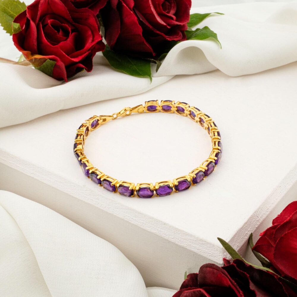 A women's bracelet with oval-cut purple amethyst gemstones in a gold-plated setting, on a white display.