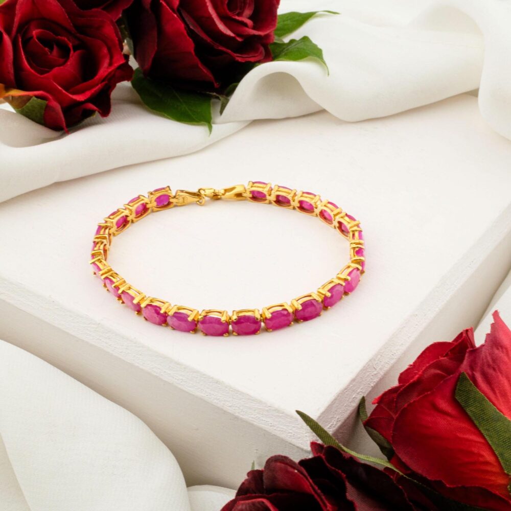 A women's bracelet with oval-cut ruby gemstones in a gold-plated sterling silver setting, on a white display.