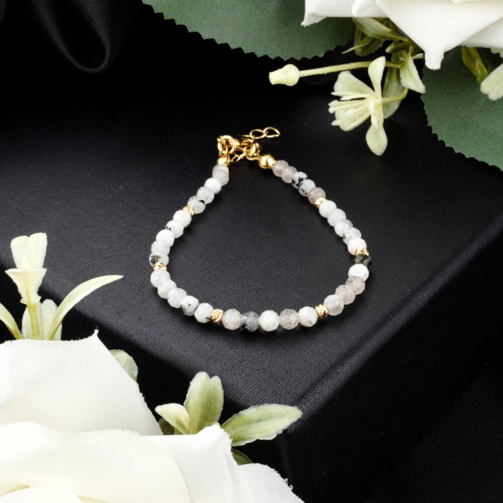 Faceted rainbow moonstone bracelet with gold-tone steel beads and adjustable clasp on black display