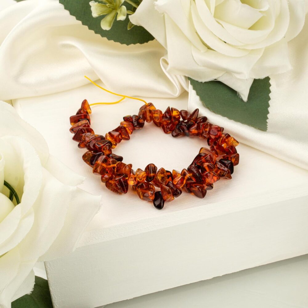 A strand of raw dark amber chips (broken rock style) on a white display