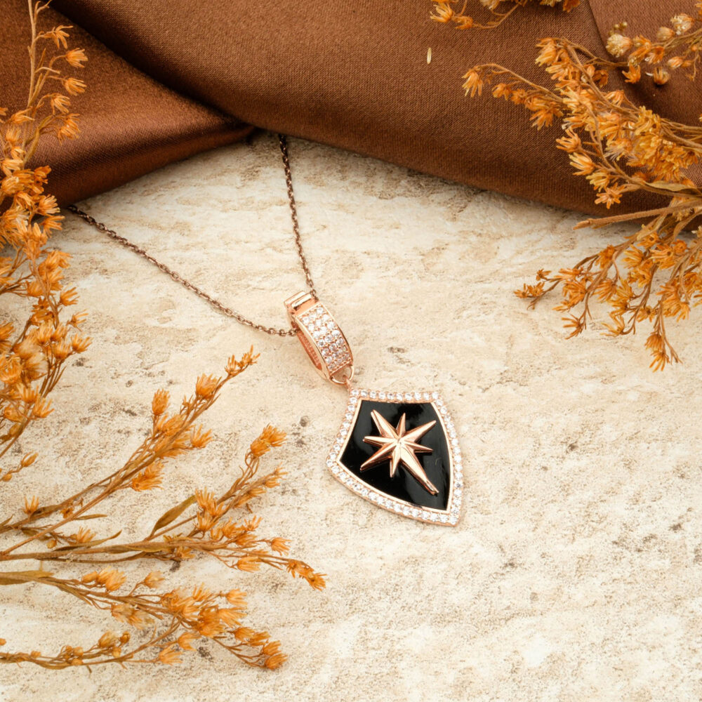 Premium rose gold-plated 925 silver North Star shield necklace with black enamel, on a brown satin background.