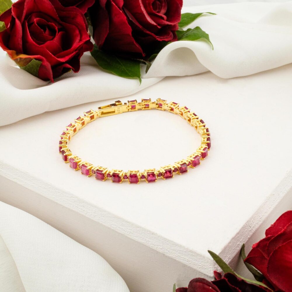 An elegant ruby tennis bracelet with square-cut stones in a gold-plated sterling silver setting, on a white display.