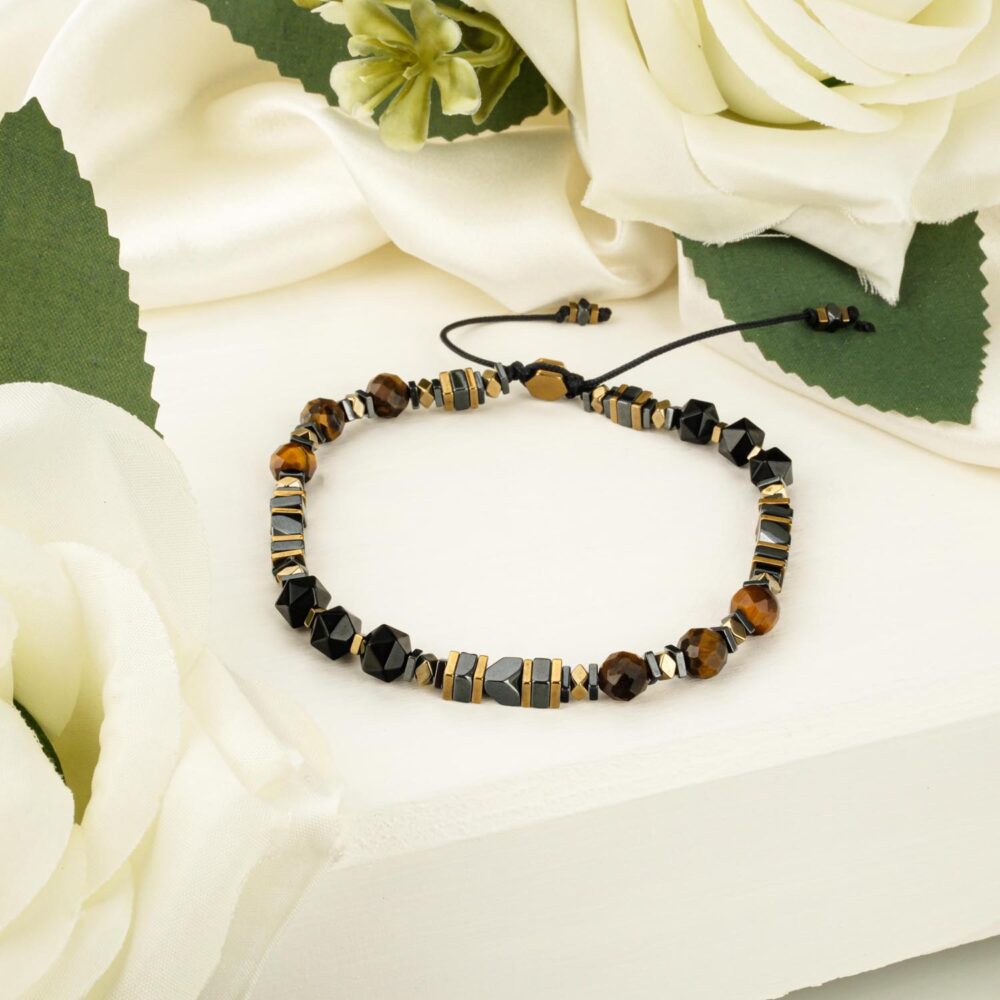A triple protection bracelet featuring faceted tiger's eye, hematite, and onyx beads on an adjustable black cord, displayed on a white surface.