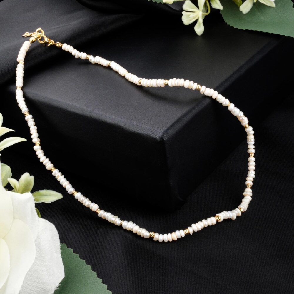 Delicate tiny freshwater seed pearl necklace with gold-tone steel beads on black display