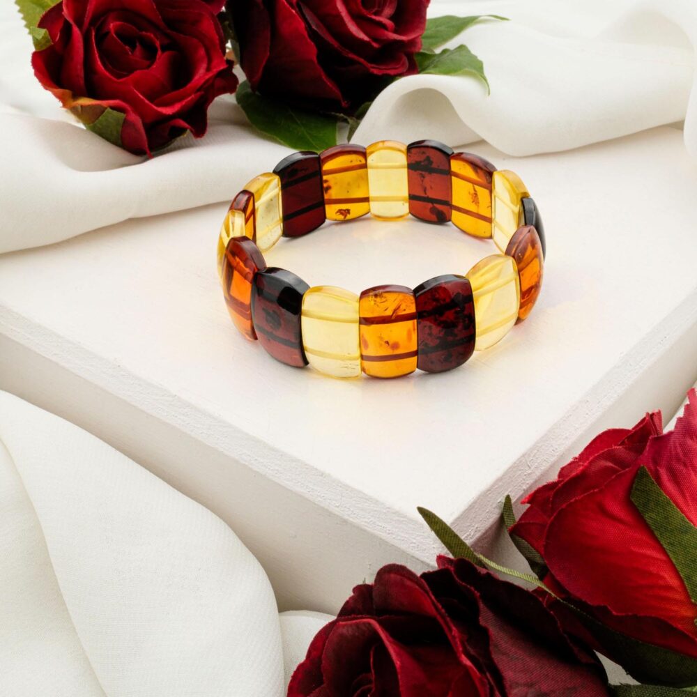 A tricolor (cherry red, lemon yellow) Baltic Amber bracelet with large, polished 'Rolex-style' links, styled on a white box with red roses.