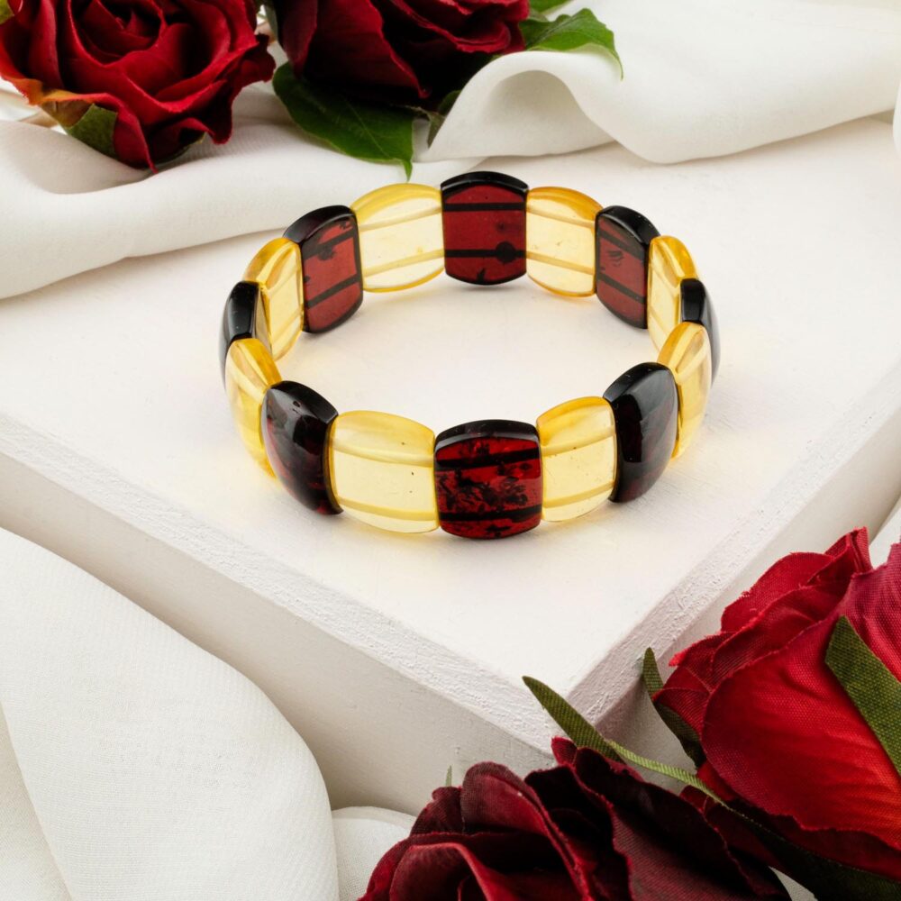 A tricolor (cherry red, lemon yellow) Baltic Amber bracelet with large, polished 'Rolex-style' links, styled on a white box with red roses.