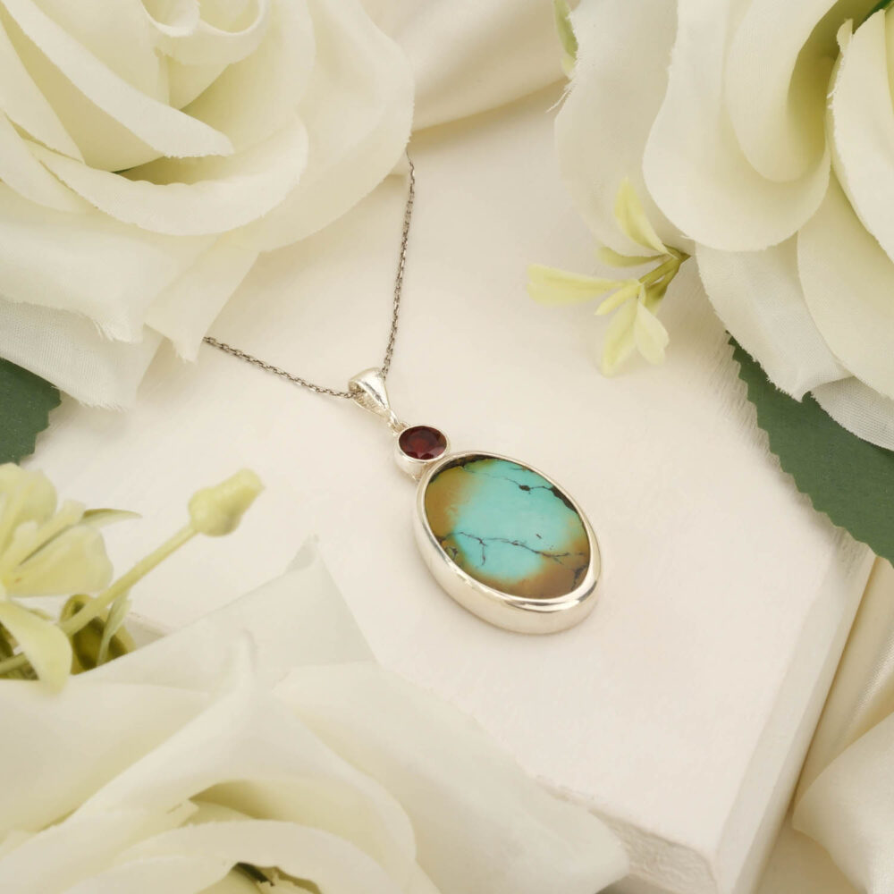 Oval turquoise and round garnet pendant necklace in 925 sterling silver on white background