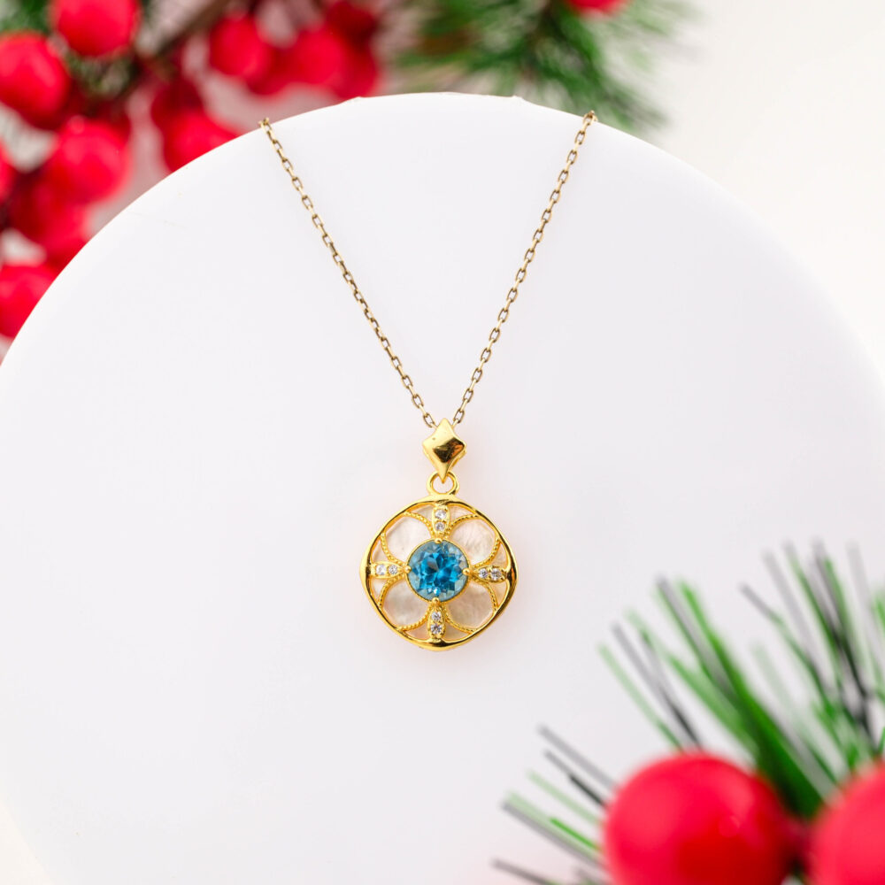 A gold-plated 925 sterling silver necklace featuring a round floral pendant with a central Blue Topaz and Mother of Pearl background.
