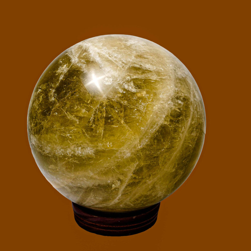 Esfera grande de cristal de cuarzo limón amarillo sobre soporte de madera con fondo de bosque