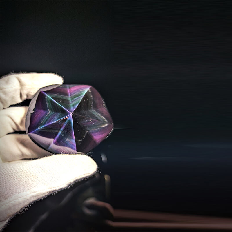 Una pieza de piedra natural de Obsidiana Arcoíris de 69,23 g que muestra vibrantes bandas de luz de color púrpura y verde en un patrón geométrico.