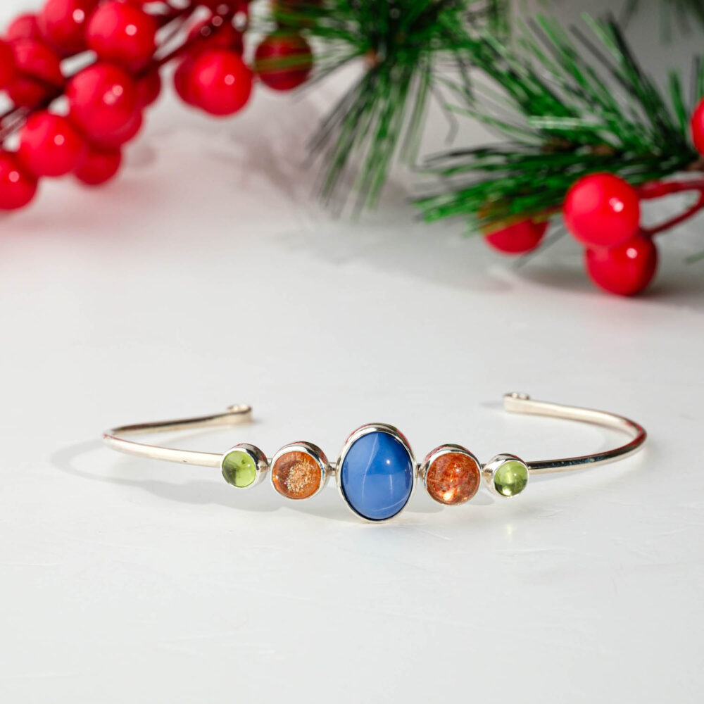 925 sterling silver cuff bracelet featuring a central oval blue star sapphire flanked by round orange sunstones and green peridots
