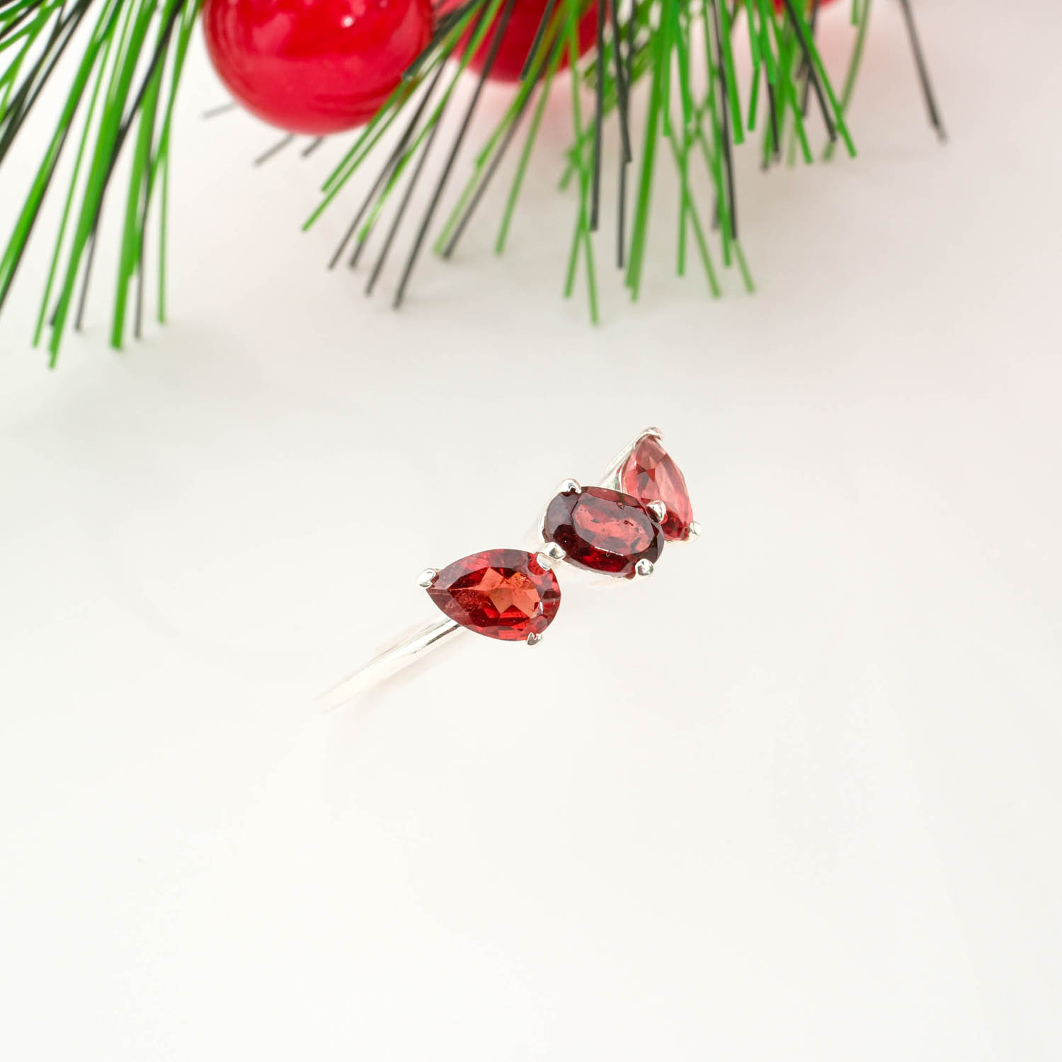 925 sterling silver trilogy ring featuring an oval center garnet flanked by two pear cut natural garnet gemstones